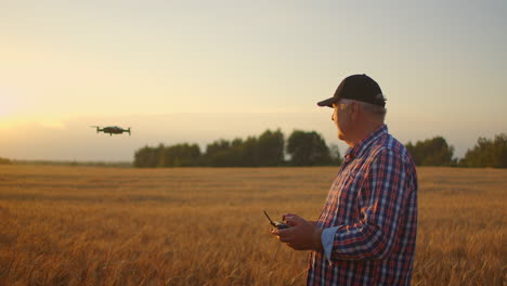 a-senior-adult-farmer-in-a-cap-uses-a-drone-to-fly-over-a-field-of-wheat.-An-elderly-farmer-uses-a-controller-to-control-the-drone.-Modern-technologies-in-agriculture